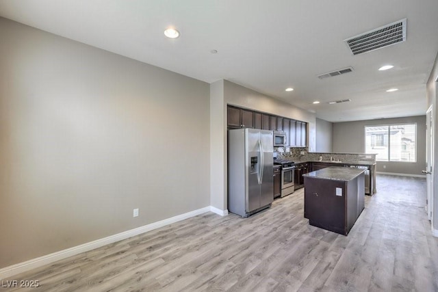 kitchen with light hardwood / wood-style flooring, appliances with stainless steel finishes, tasteful backsplash, a kitchen island, and dark brown cabinetry