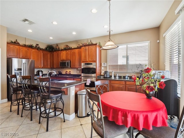 kitchen with a kitchen island, stainless steel appliances, hanging light fixtures, light tile patterned flooring, and a breakfast bar area