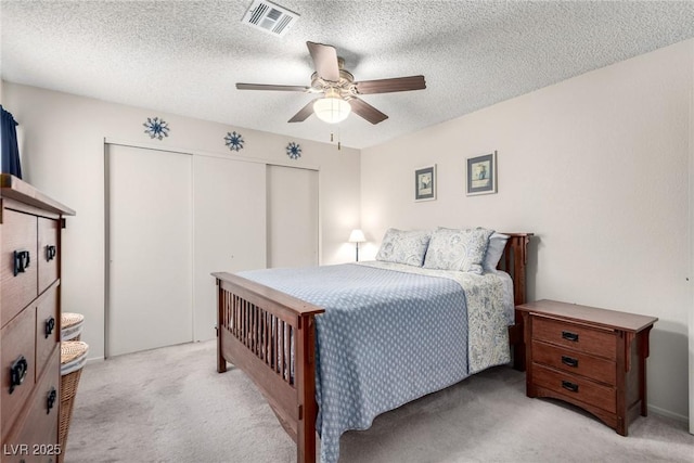 bedroom featuring a closet, a textured ceiling, light colored carpet, and ceiling fan