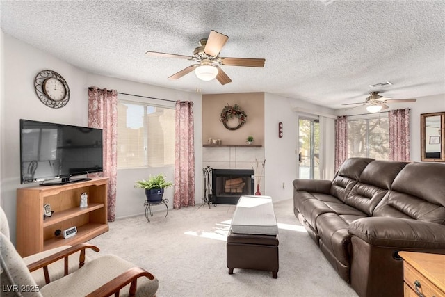 living room with a textured ceiling, ceiling fan, light carpet, and a tile fireplace