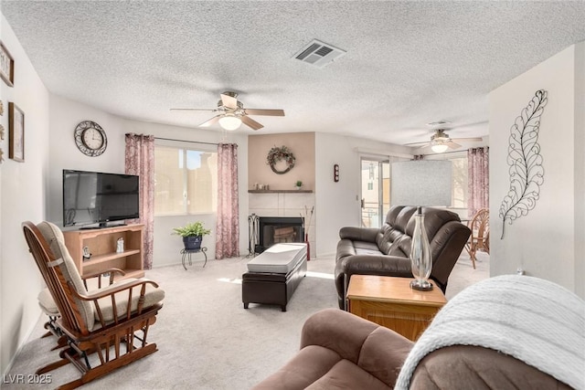 living room featuring a tiled fireplace, ceiling fan, carpet floors, and a textured ceiling