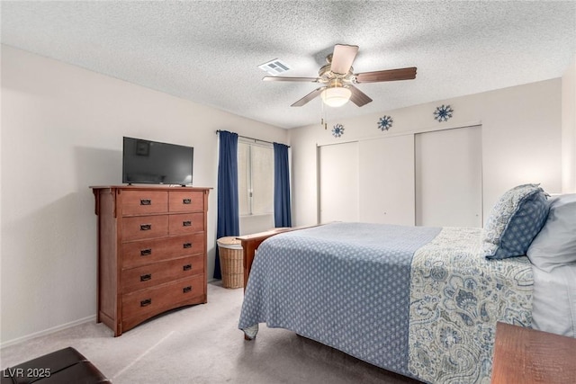 bedroom with a textured ceiling, ceiling fan, light carpet, and a closet