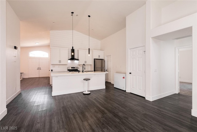 kitchen featuring a kitchen island with sink, appliances with stainless steel finishes, wall chimney exhaust hood, white cabinetry, and decorative light fixtures