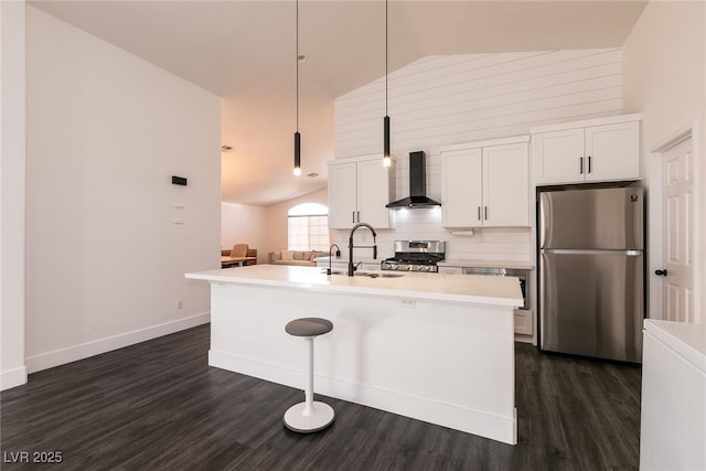 kitchen featuring stainless steel appliances, wall chimney range hood, white cabinets, and an island with sink