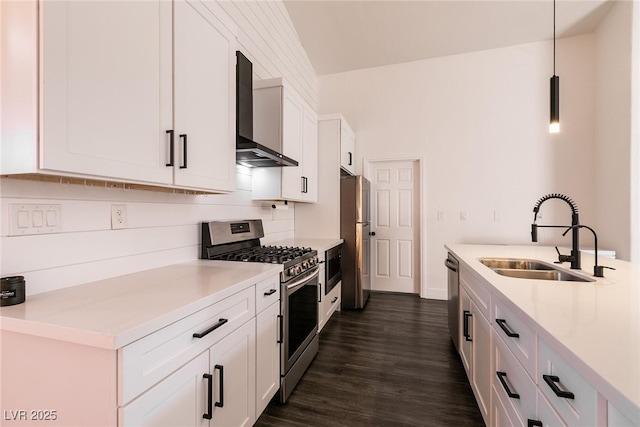 kitchen with decorative light fixtures, stainless steel appliances, wall chimney range hood, white cabinets, and sink