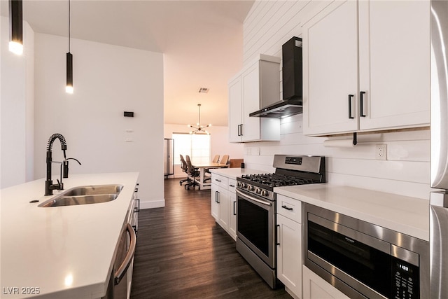 kitchen with stainless steel appliances, white cabinetry, hanging light fixtures, and wall chimney exhaust hood