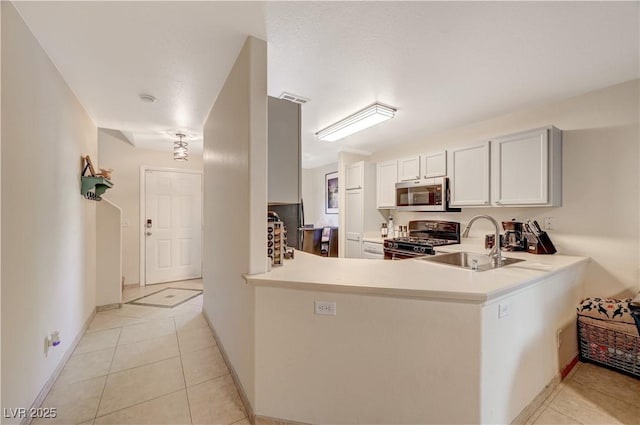 kitchen featuring sink, range with gas cooktop, light tile patterned floors, kitchen peninsula, and white cabinets