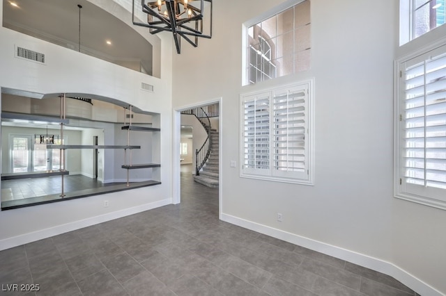 unfurnished living room with tile patterned floors, a healthy amount of sunlight, a high ceiling, and a notable chandelier