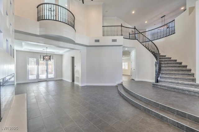 tiled entrance foyer with a notable chandelier, a towering ceiling, crown molding, and french doors