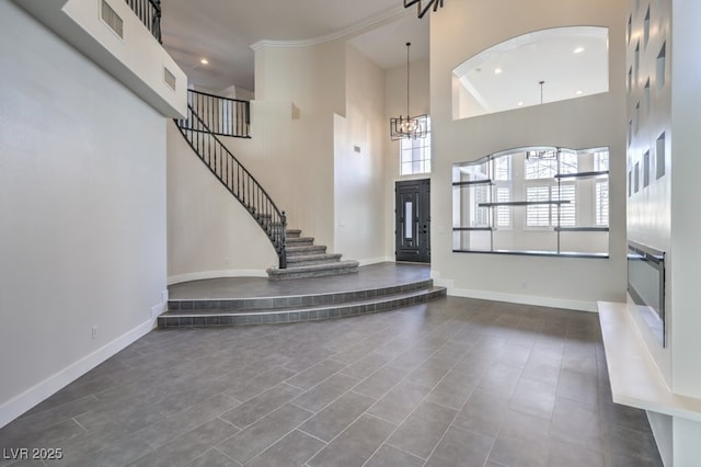 foyer with crown molding, dark tile patterned floors, a high ceiling, and a notable chandelier