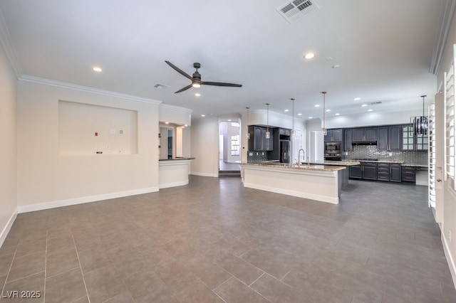 kitchen with a center island with sink, sink, tasteful backsplash, decorative light fixtures, and light stone counters