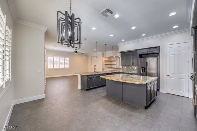 kitchen featuring light stone countertops, high quality fridge, ornamental molding, decorative light fixtures, and a center island