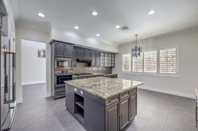 kitchen with light stone countertops, stainless steel appliances, tasteful backsplash, decorative light fixtures, and a kitchen island