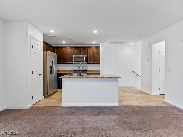 kitchen with light carpet, a center island with sink, appliances with stainless steel finishes, light stone countertops, and sink