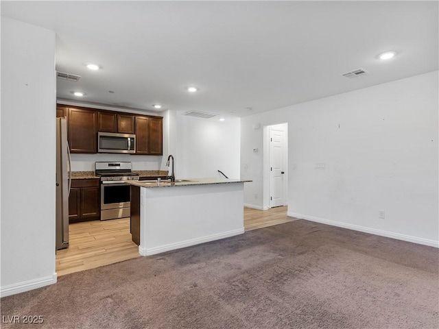 kitchen with light stone counters, a kitchen island with sink, appliances with stainless steel finishes, light carpet, and sink