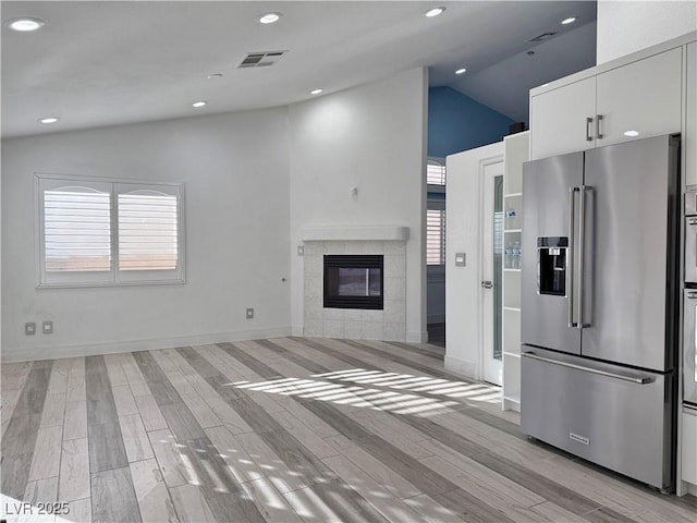 kitchen featuring white cabinets, high end refrigerator, lofted ceiling, and a tiled fireplace