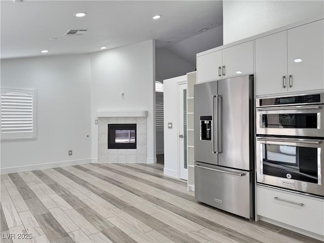 kitchen with white cabinetry, stainless steel appliances, a tiled fireplace, and light hardwood / wood-style floors