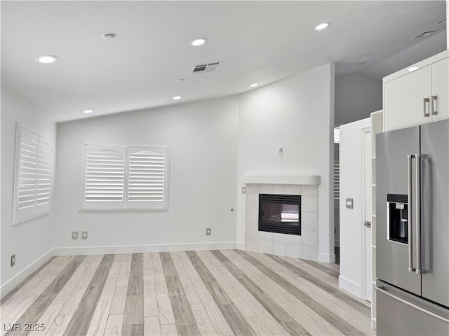 unfurnished living room featuring vaulted ceiling, a tile fireplace, and light wood-type flooring