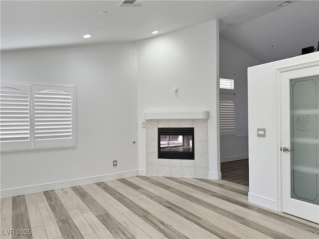 unfurnished living room featuring vaulted ceiling, light hardwood / wood-style floors, and a tile fireplace