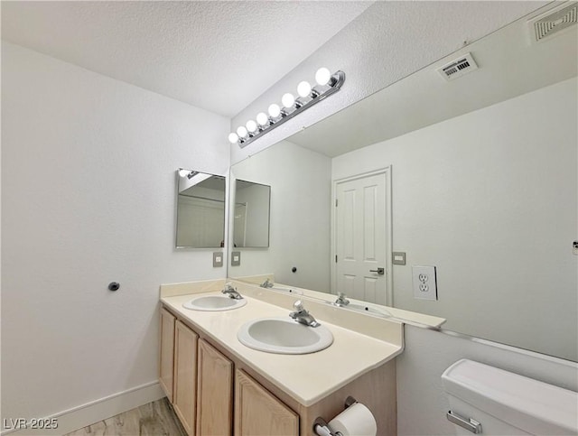 bathroom featuring wood-type flooring, vanity, a textured ceiling, and toilet