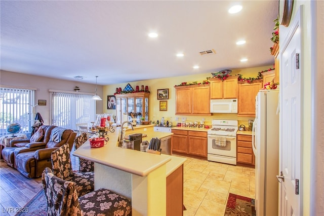 kitchen featuring a kitchen bar, sink, white appliances, and decorative light fixtures