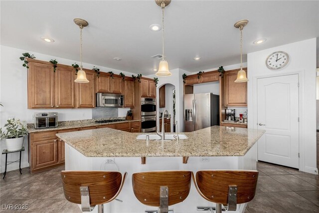 kitchen with appliances with stainless steel finishes, light stone counters, sink, a large island with sink, and pendant lighting