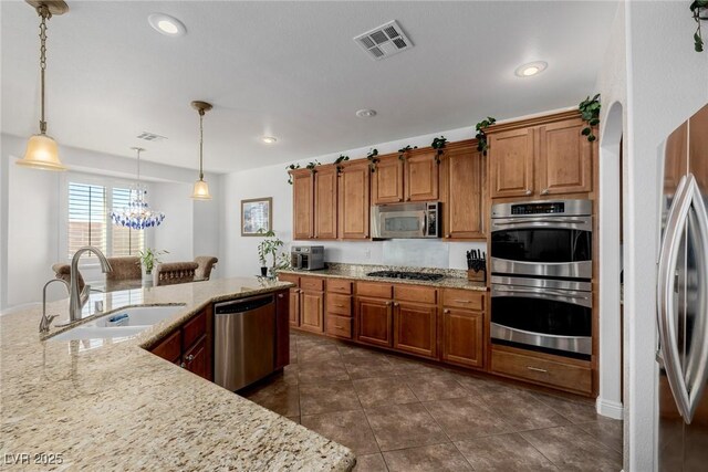 kitchen with sink, hanging light fixtures, appliances with stainless steel finishes, light stone counters, and a chandelier