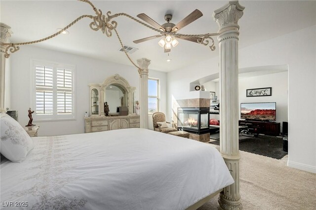 carpeted bedroom featuring a fireplace, ornate columns, and ceiling fan