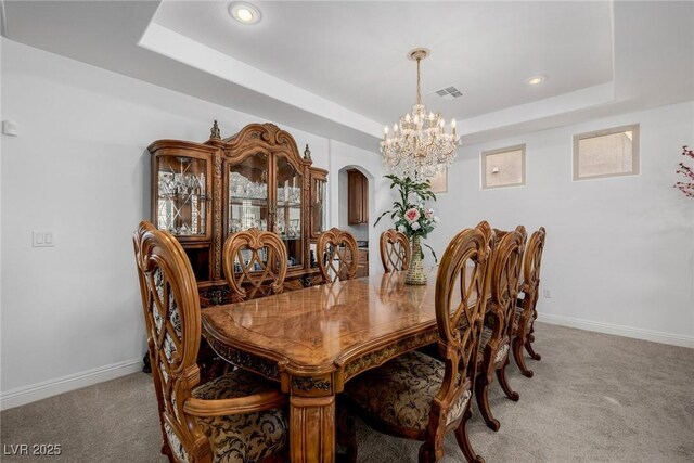 carpeted dining area with a chandelier and a tray ceiling