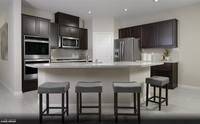 kitchen with decorative backsplash, light tile patterned floors, stainless steel appliances, and an island with sink