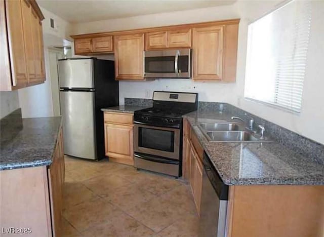 kitchen featuring stainless steel appliances, light tile patterned flooring, sink, and dark stone counters