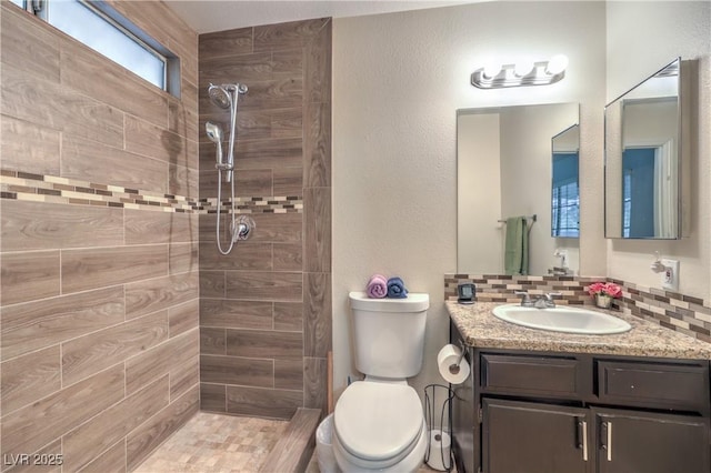 bathroom featuring vanity, toilet, backsplash, and a tile shower