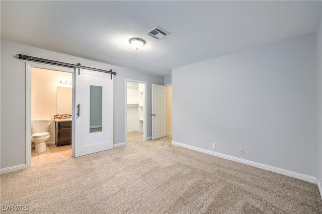 unfurnished bedroom with light carpet, ensuite bathroom, a walk in closet, a barn door, and a closet