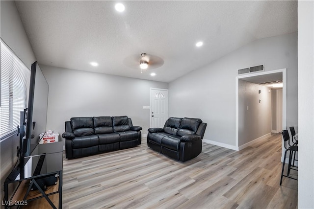 living room featuring a textured ceiling, light wood-type flooring, vaulted ceiling, and ceiling fan