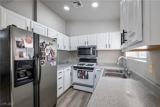 kitchen with appliances with stainless steel finishes, sink, light hardwood / wood-style flooring, white cabinetry, and lofted ceiling