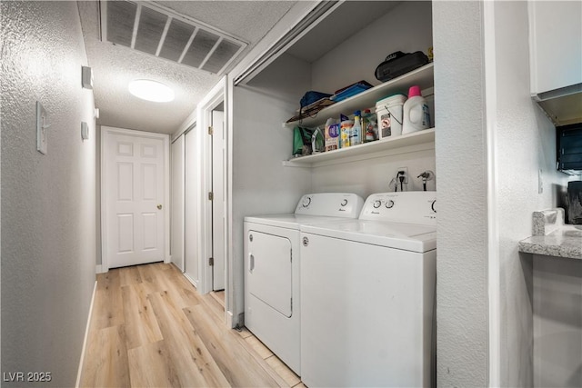 washroom with a textured ceiling, light hardwood / wood-style floors, and washer and clothes dryer