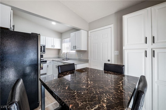 kitchen featuring stainless steel appliances, sink, dark stone countertops, white cabinetry, and lofted ceiling