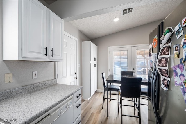 kitchen with french doors, white cabinets, vaulted ceiling, light hardwood / wood-style flooring, and a textured ceiling