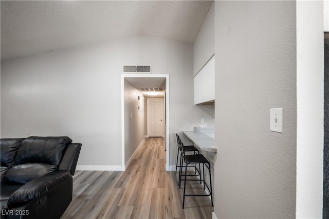 corridor featuring a textured ceiling, light hardwood / wood-style floors, and lofted ceiling