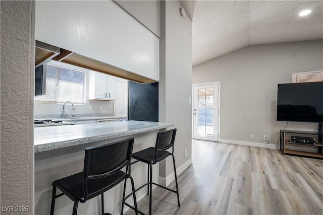 kitchen featuring lofted ceiling, white cabinets, a textured ceiling, light hardwood / wood-style floors, and light stone counters