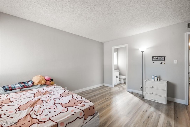 bedroom with ensuite bathroom, a textured ceiling, and light hardwood / wood-style flooring