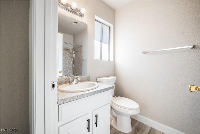 bathroom with hardwood / wood-style floors, vanity, toilet, and tiled shower