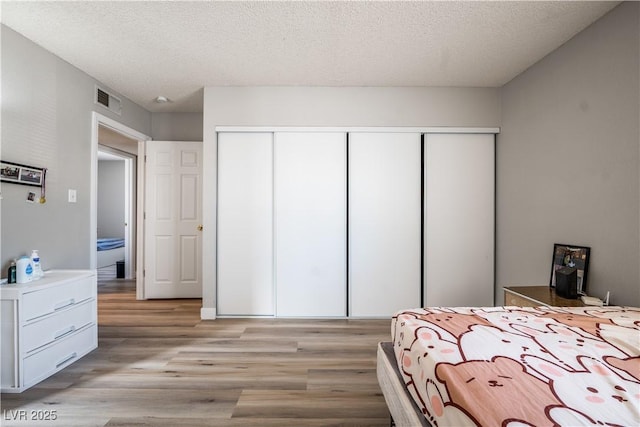 bedroom with a textured ceiling, light hardwood / wood-style flooring, and a closet