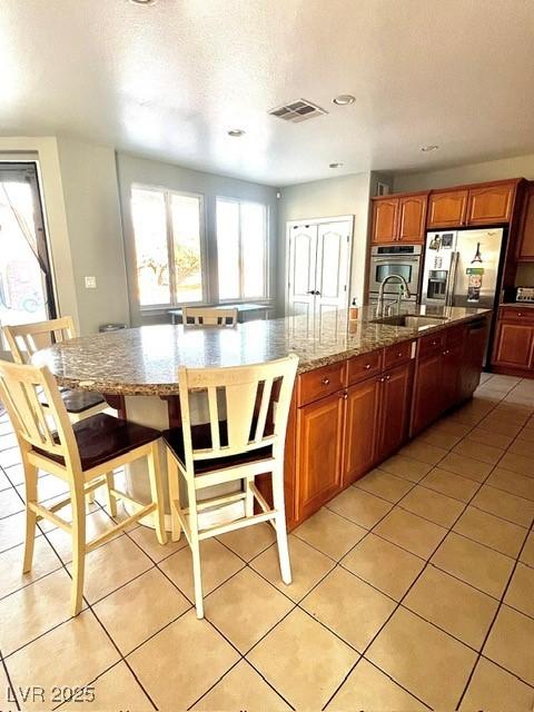 kitchen featuring a kitchen island with sink, sink, light tile patterned floors, and stainless steel appliances