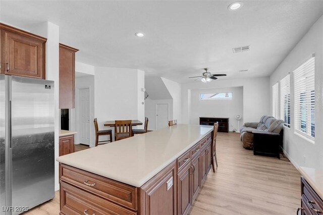 kitchen with a center island, ceiling fan, stainless steel fridge, light wood-type flooring, and a fireplace