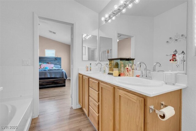 bathroom with hardwood / wood-style flooring, vanity, a tub, and vaulted ceiling