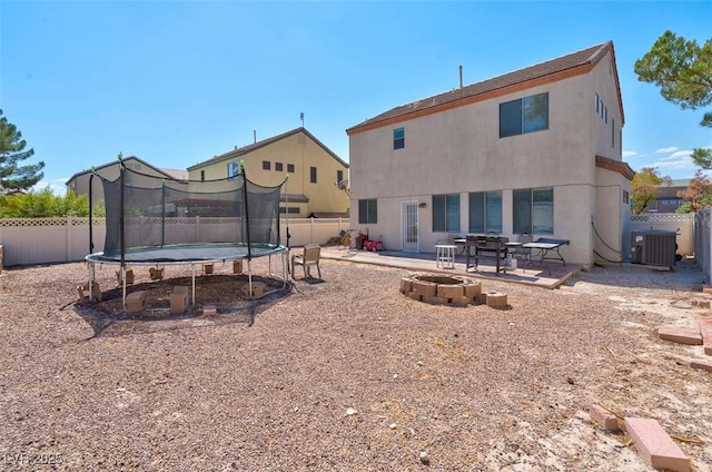 back of property with cooling unit, a trampoline, an outdoor fire pit, and a patio area