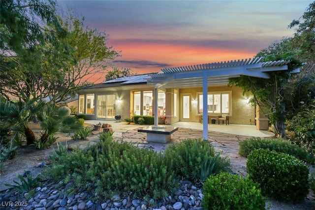 back house at dusk featuring a pergola, a patio area, and solar panels