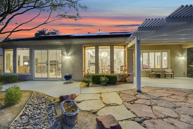 back house at dusk featuring a pergola, a patio, and solar panels