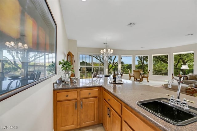 kitchen featuring stone countertops, decorative light fixtures, sink, a notable chandelier, and kitchen peninsula